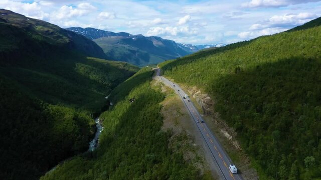 Aerial view overlooking cars and campers driving on a mountain road, Arctic fells in the background, sunny day, in Nordland, North Norway - rising, drone shot