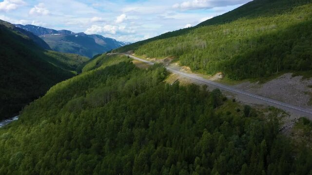 Aerial view of a asphalt, mountain road, Arctic fells in the background, sunny day, in Nordland, North Norway - rising, drone shot