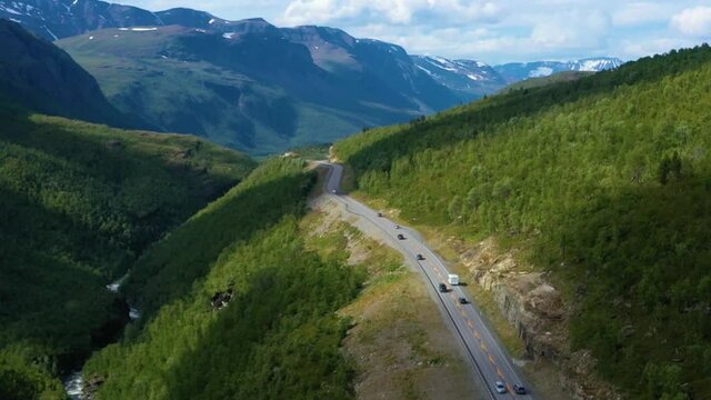 Aerial view overlooking RV and cars, driving on a mountain road, Arctic fells in the background, sunny day, in Norway - rising, drone shot