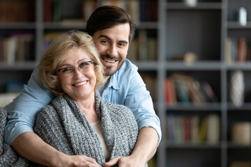 Head shot portrait smiling mature woman and young man hugging, looking at camera, loving adult son...