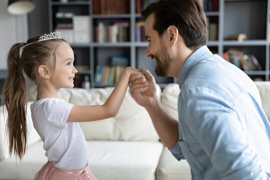 Close Up Loving Father Holding Adorable Little Daughter Hand, Pretty Girl Wearing Princess Dress And Diadem Playing With Dad, Family Enjoying Tender Moment, Leisure Time At Home Together