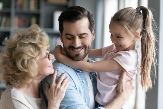 Close up smiling young man with pretty little girl and mature mother wearing glasses enjoying tender moment, hugging, loving father holding adorable daughter, happy family, three generations