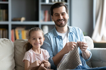 Head shot portrait smiling father and little girl knitting together, looking at camera, positive...
