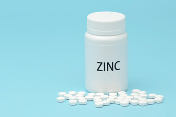 ZINC in white bottle packaging with scattered pills. Nutritional supplement. Treatments for COVID-19. isolated on blue background. Horizontal shot. Copy space.