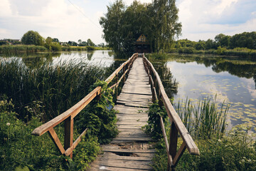 Landscape view of Old small wooden bridge across the lake. Fishman house on an island surrounded by wather and forest