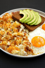 Tasty Homemade Fried Hashbrowns and Eggs on a plate on a black background, low angle view. Close-up.