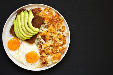 Tasty Homemade Fried Hashbrowns and Eggs on a plate on a black background, top view. Flat lay, overhead, from above. Copy space.