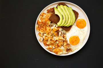 Tasty Homemade Fried Hashbrowns and Eggs on a plate on a black background, top view. Copy space.