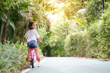 Asian child or kid girl smile and biker to cycling fun on bike or people riding bicycles on public park or garden and green tree with road of bicycle for sport exercise to healthy on family holiday
