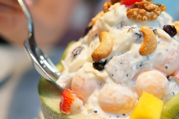 fruits salad mix with cantaloupe strawberry mango kiwi cashew nuts cherry and dragon fruit in cantaloupe shell bowl with spoon for diet juicy dessert and vitamins food nutrition on warm white