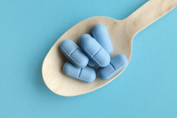 Close up of blue pills, tablets in a wooden spoon on a blue table. Medicine and health concept. pharmaceuticals. View from above. Tablets and vitamins