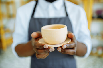 mixed race afro male potter with black apron sitting at workshop table potter