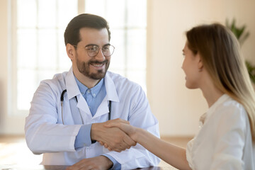 Obraz premium Close up smiling doctor therapist gp wearing white medical uniform and glasses shaking patient hand at meeting in hospital, getting acquaintance, making healthcare insurance deal, agreement