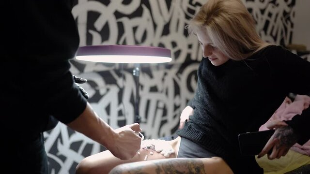
tattoo artist sprays foam on the leg of a young woman where he made a tattoo for styling