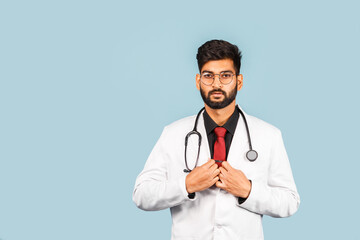 Fototapeta premium Cute Indian / Asian doctor wearing glasses with stethoscope, tie and white coat on light blue background.