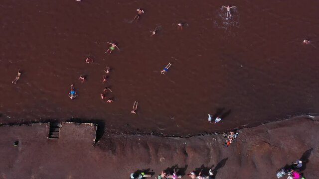 Aerial top down shot of a thalassotherapy salt lake with swimmers floating in the salty brown pond. Pedra de Lume salt evaporation ponds inside the crater of an extinct volcano. Cape Verde.