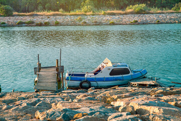 old wooden boat and pier next to the rocks in the riverside at sunset