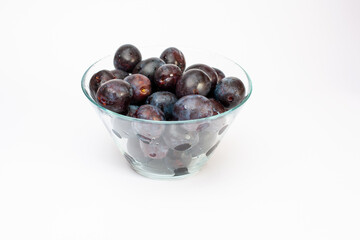 plums in a glass bowl on a white background. Ripe blue plums in a transparent dish