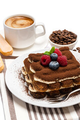 portion of Classic tiramisu dessert with raspberries, blueberries and cup of fresh hot espresso isolated on white background - clipping path