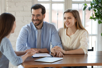 Happy young married couple listening to realtor or financial advisor at meeting, smiling man and...