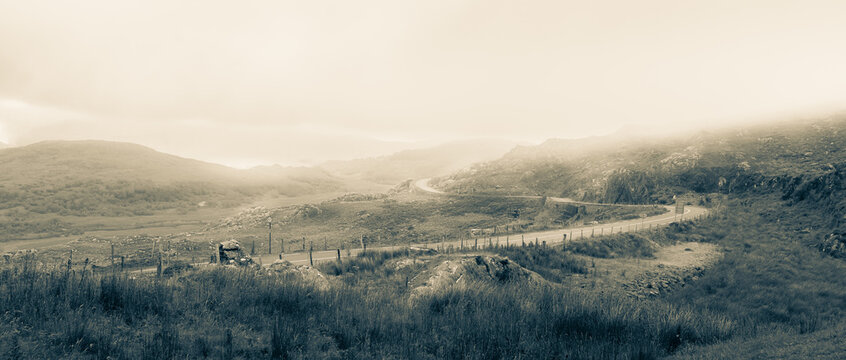 Monochrome Image Of The Misty Hills Of Molls Gap In Kerry, Ireland. The Narrow Windy Road Disappears In To The Fog.