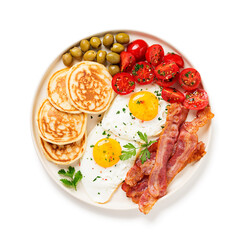 American breakfast with two fried eggs,pancakes,tomato salad,bacon and green olives. isolated on white background. top view