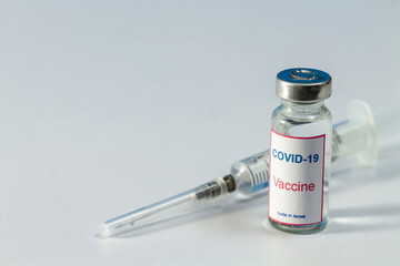 In the foreground is a bottle containing the COVID-19 vaccine with the words 