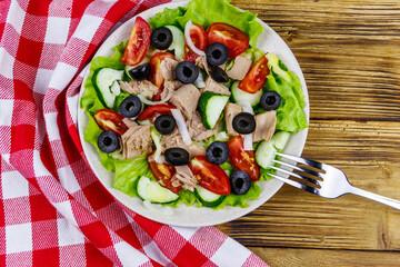 Tasty tuna salad with lettuce, black olives and fresh vegetables on wooden table. Top view
