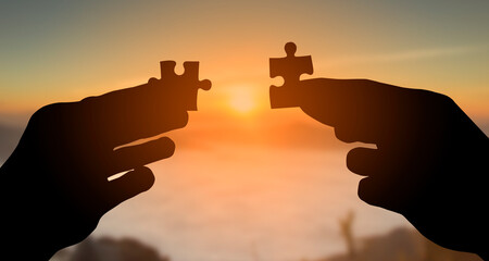silhouette of hands holding jigsaw puzzle and raised to joining at sunrise,  Teamwork, partnership and community concept
