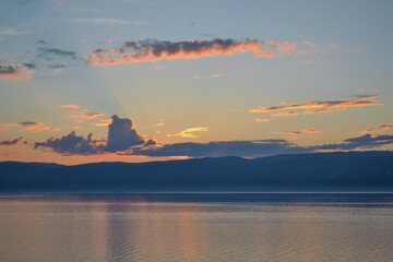 view of the clear calm undulating blue water of Lake Baikal, mountains on the horizon, sunset yellow, pink light, clouds