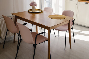 Wooden dining table with four pink plastic chairs around it and a pink flower standing on it in a modern style kitchen on a sunny day