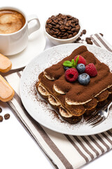 portion of Classic tiramisu dessert with raspberries, blueberries and cup of fresh hot espresso isolated on white background - clipping path