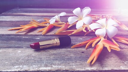 Red matte lipstick,Heliconia flower,and Frangipani flowers,on old wood.Rustic still life,soft dark...