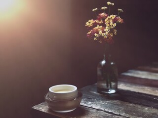 Facial cosmetic cream container and Heliconia flower,Frangipani flowers,on old wood plank.Rustic still life,soft dark tone,dimly light,with lens flare,free space for your text design or your products.