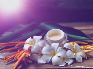 Fototapeta na wymiar Facial cosmetic cream container and Heliconia flower,Frangipani flowers,on old wood plank.Rustic still life,soft dark tone,dimly light,with lens flare,free space for your text design or your products.