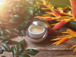 Obraz na płótnie Canvas Facial cosmetic cream container and Heliconia flower,Frangipani flowers on old wood plank.Rustic still life,soft dark tone,dimly light,with lens flare,free space for your text design or your products.