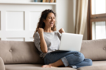 Woman sit on sofa put pc on lap clenched fists scream with joy while read great news on laptop....