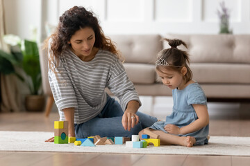 Little girl play with colourful toy blocks set sit on wooden warm heated floor in playroom with mom or woman babysitter, educational game, family at home spend leisure activities time together concept