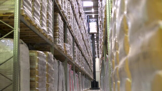 Forklift moving wooden pallet to top of industrial storage area/warehouse