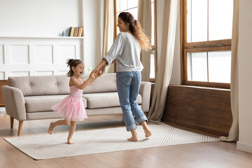 Little princess in fluffy pink dress tiara on head hold hands with mum while dance barefoot enjoy...