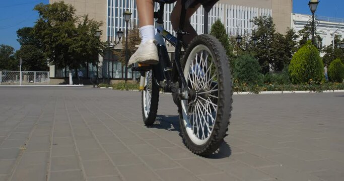 Unrecognizable girl  riding a bicycle along the city street wearing  striped shorts, white snickers and white T-shirt. Close up legs and bicycle. 50 fps slow motion 4k