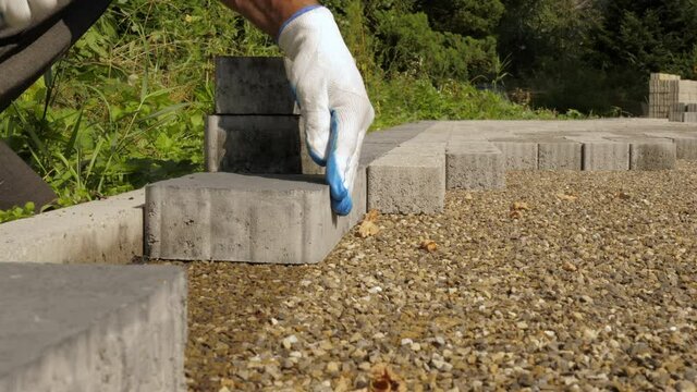 Construction worker. Hands of a master bricklayer are laying the paving slabs. The builder makes a sidewalk in a city park. Low-angle view
