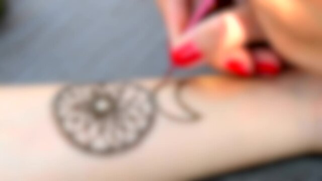 Blurred background. Drawing mehendi Dreamcatcher on a hand close-up.