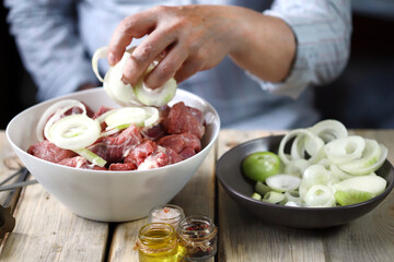 Soft focus. The chef prepares meat for barbecue. Pieces of meat in a bowl. Raw onion rings.