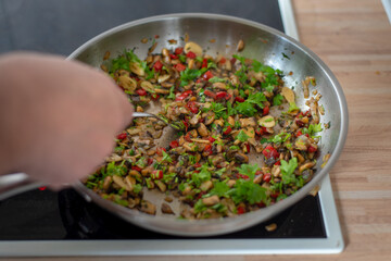 fried paprika and onions on a hot frying pan sprinkled with parsley, preparing a meal at home