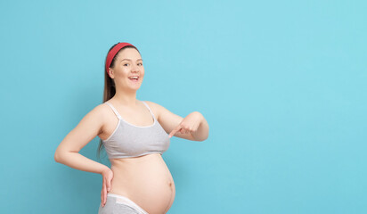 happy young pregnant woman on blue background, woman points finger to belly
