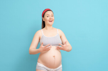 young pregnant woman is surprised that her breasts have grown on blue background