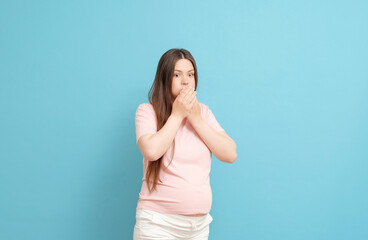 young pregnant woman in pink t-shirt on blue background, toxicosis during pregnancy