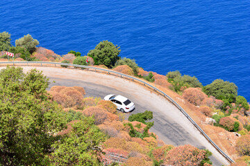Fototapeta premium Car rental during the travel concept. White car driving by the serpentine road over the sea. Beautiful mediterranean landscape.