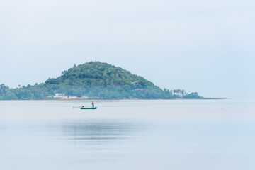 alone fisherman in a boat pulls a net, fishing on a tropical samui island in thailand, early foggy morning